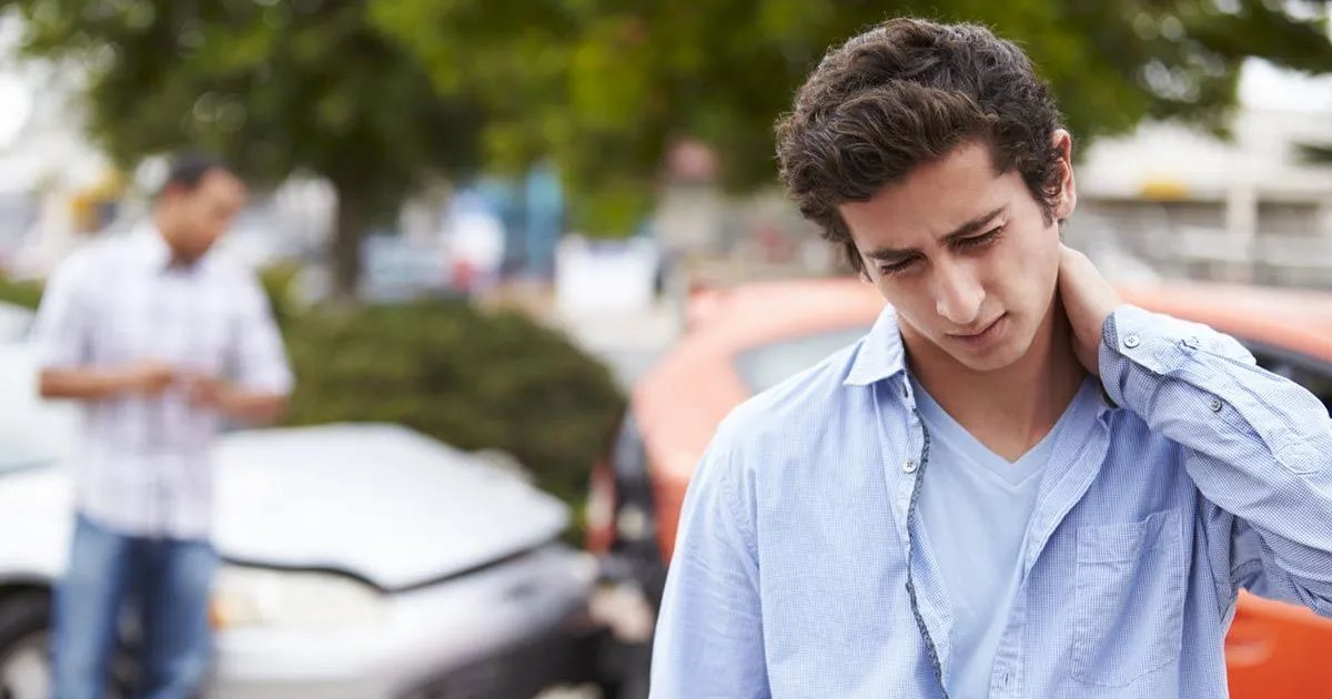 A young man holding the back of his neck beside two cars after a rear-end collision